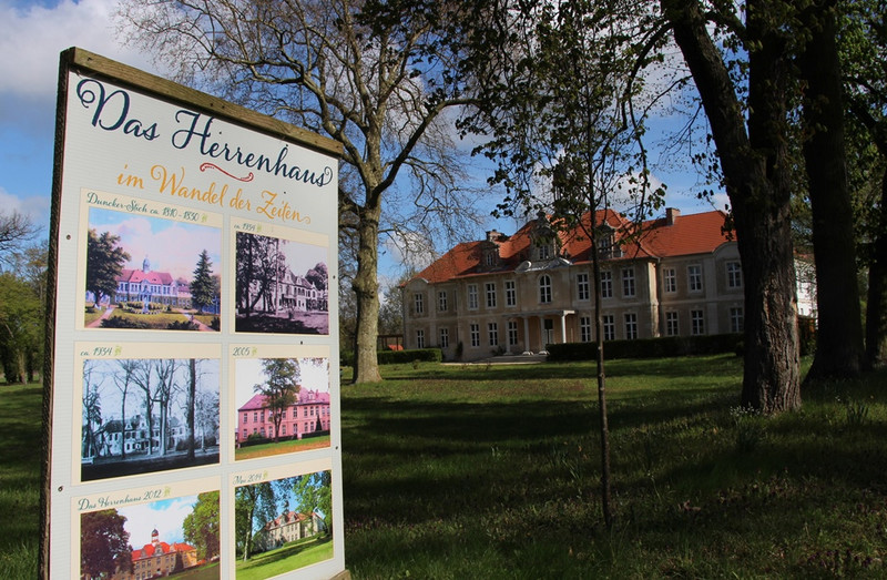Informationstafel über das Herrenhaus Karow im Wandel der Zeiten, im Hintergrund das Herrenhaus