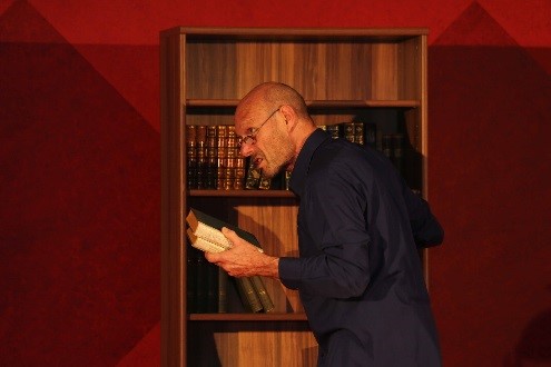 Schauspieler nimmt Bücher aus einem Regal auf der Bühne