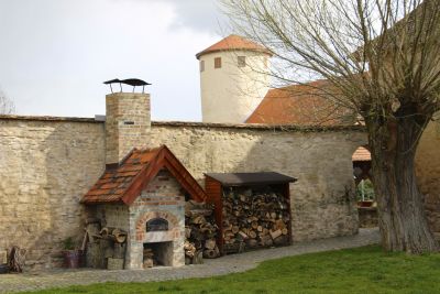 Burghof mit Kaminofen und aufgestapeltem Kaminholz, im Hintergrund der Burgturm, der alles überragt