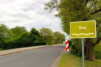 Straße über eine Brücke, Rechts im Bild ein Schild mit dem Hinweis auf den Fluss Ilse