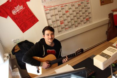 Ein junger Mann sitzt in einem Büro und spielt Gitarre. Bild: Ministerium der Finanzen des Landes Sachsen-Anhalt