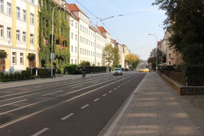 Auf dem Foto sieht man eine Straße mit Straßenbahngleisen, einigen Autos und einem Fahrradfahrer. Links und rechts stehen Wohnhäuser. (Foto: Ministerium der Finanzen LSA)