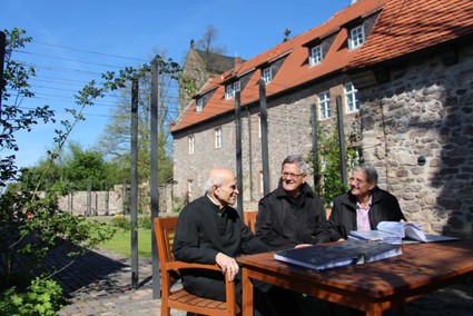 The picture shows three men conversing on a bench in front of an old building. (Picture: Ministry of Finance of Saxony-Anhalt)