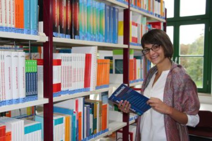 The picture shows a young lady in front of a book shelf. (Picture: Ministry of Finance of Saxony-Anhalt)