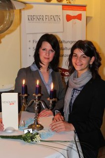 The picture shows two young women standing at a bar table adorned with a three-armed candelabra and its burning candles. (Picture: Ministry of Finance of Saxony-Anhalt)