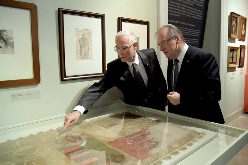 Das Bild zeigt links den für Kultur zuständigen ungarischen Minister Balog, der mit ausgestrecktem Arm Ministerpräsident Haseloff ein in einer Glasvitrine liegendes Exponat der Ausstellung.