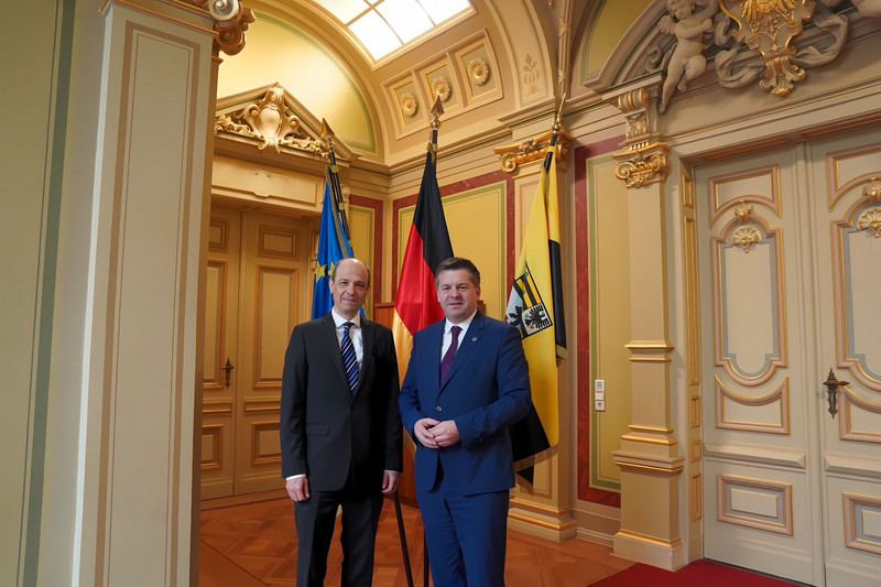 Beide Männer stehen nebeneinander in einem Raum der Staatskanzlei. In Hintergrund sind Fahnen zu sehen.