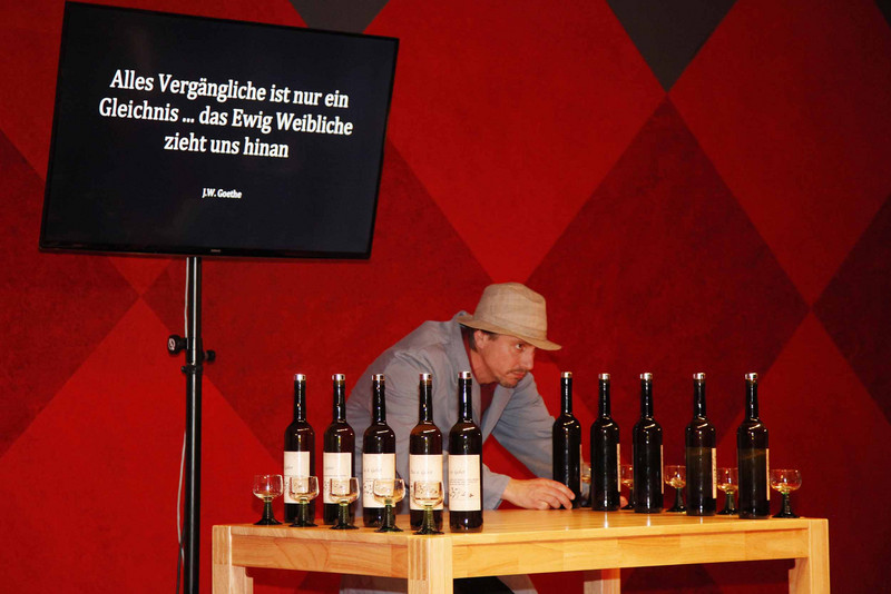 Schauspieler steht während der Aufführung hinter einem Tisch mit Flaschen und Gläsern