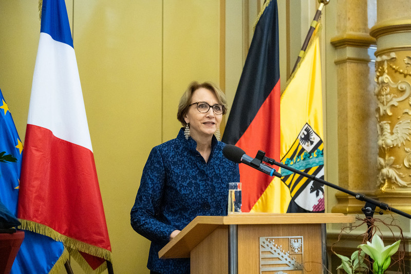 Das Foto zeigt Botschafterin Descotes am Rednerpult vor den Flaggen Frankreichs, Deutschlands und Sachsen-Anhalts.