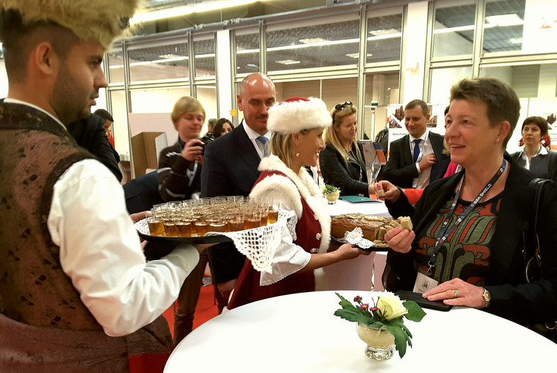 Das Bild zeigt einen Mann in traditioneller polnischer Kleidung mit einem Tablett und Ministerin Dalbert, die vom dargereichten Brot und Salz probiert. Das Bild entstand am Stand der Wojewodschaft Masowien.