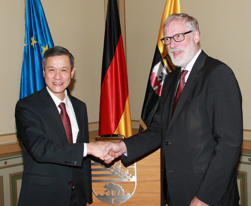 Das Bild zeigt links Botschafter Nguyen und rechts Staatsminister Robra beim Handschlag vor den Flaggen der EU, Deutschlands und Sachsen-Anhalts.