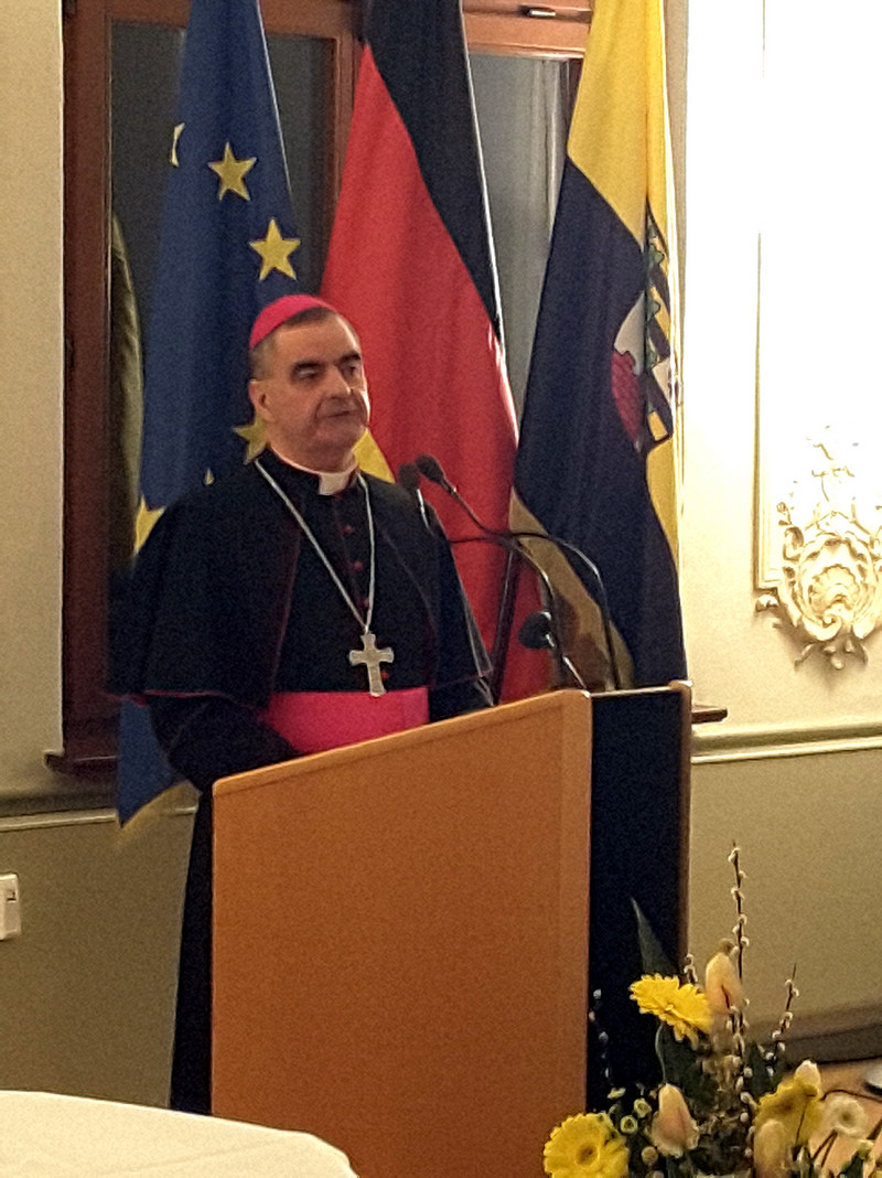 Das Bild zeigt den Apostolischen Nuntius bei seiner Ansprache an einem Rednerpult vor den Fahnen der EU, Deutschlands und Sachsen-Anhalts.