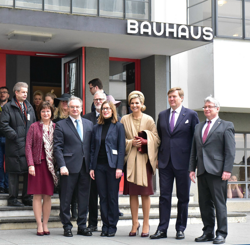 Das Bild zeigt das Königspaar mit Ministerpräsident Haseloff, dessen Gattin, Kulturminister Robra, der Direktorin der Stiftung Bauhaus Dessau, Perren, und Dessau-Roßlaus Oberbürgermeister Kuras vor dem Eingang mit dem Schriftzeug Bauhaus.