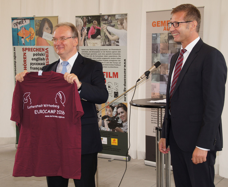 Das Bild zeigt links Ministerpräsident Haseloff, der das offizielle T-Shirt zum Eurocamp 2016 präsentiert, das ihm der Vorsitzende der Auslandsgesellschaft Sachsen-Anhalt, Krzysztof Blau (rechts im Bild) überreicht hat