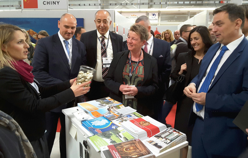 Das Bild zeigt Ministerin Dalbert mit Ehrengästen am Stand Sachsen-Anhalts. Eine Standbetreuerin reicht Hallorenkugeln.