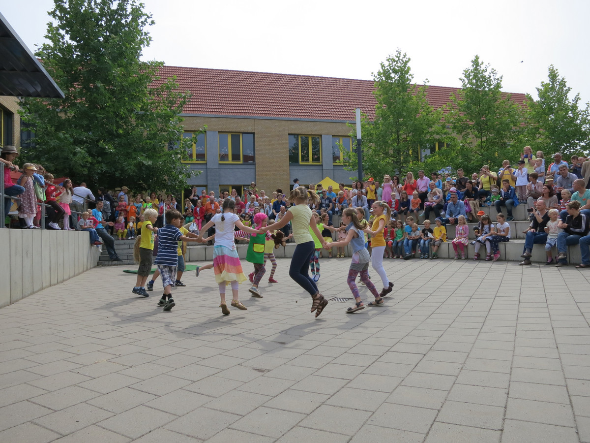 Das Foto zeigt die im Kreis spielenden Kinder auf dem Schulhof der