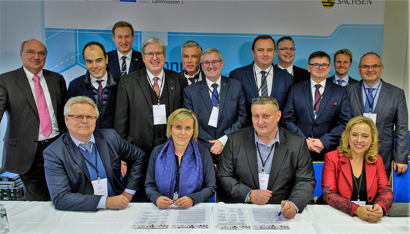 Das Bild zeigt Wirtschaftsstaatssekretär Dr. Jürgen Ude (Mitte) mit weiteren, teilweise sitzenden, teilweise stehenden Vertreterinnen und Vertretern aus 13 anderen europäischen Kohleregionen bei der Unterzeichnung der „Görlitzer Erklärung“ im November 2019. Auf dem Tisch liegen zwei Exemplare der unterzeichneten Erklärung.