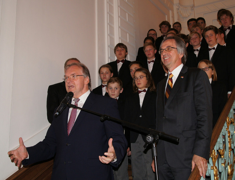 Das Bild zeigt auf einer Treppe links Ministerpräsident Reiner Haseloff bei seiner Rede, rechts Botschafter Dirk Brengelmann und dahinter den Stadtsingechor Halle.
