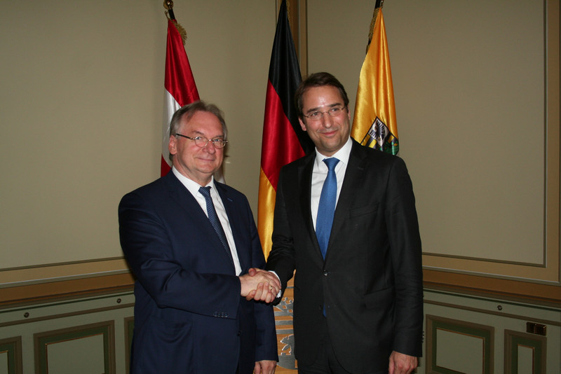 Das Bild zeigt links Ministerpräsident Reiner Haseloff und rechts Botschafter Nikolaus Marschik vor den Fahnen Österreichs, der EU und Sachsen-Anhalts.