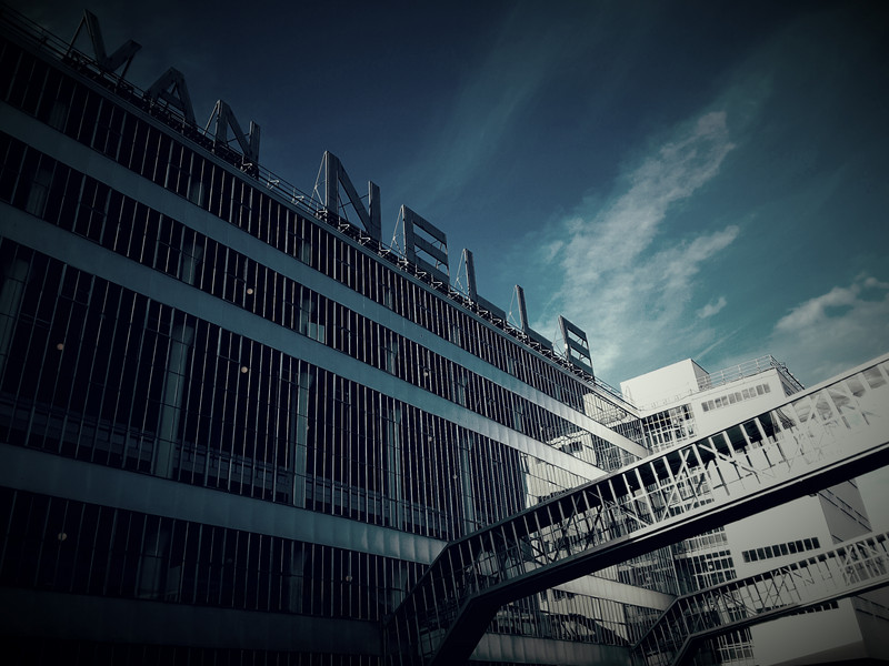 Das Bild zeigt die Glasfassade der Van-Nelle-Fabrik mit dem historischen Schriftzug "Van Nelle" auf dem Dach.