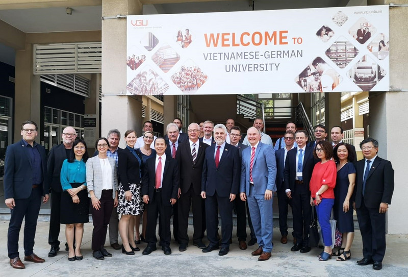Das Bild zeigt eine Delegation mit Wirtschaftsminister Armin Willingmann in der Mitte vor einem Gebäude stehend, das mit einem großen Banner geschmückt ist, welches die Besucher in englischer Sprache in der vietnamesisch-deutschen Universität willkommen heißt.