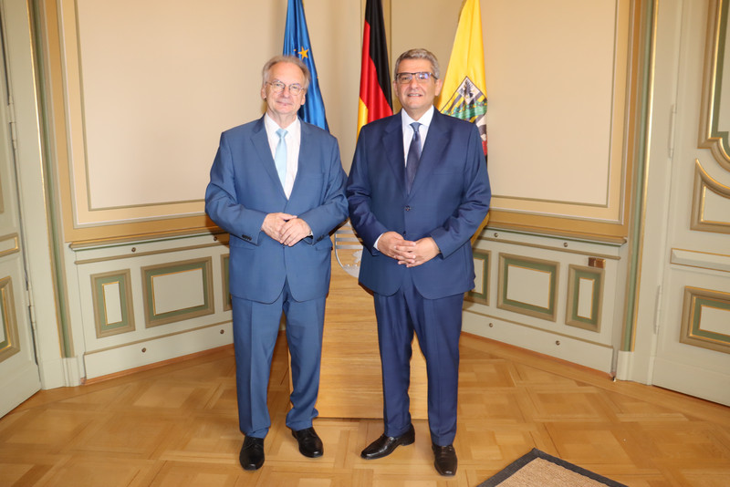 Links steht Ministerpräsident Dr. Reiner Haseloff in einem blauen Anzug und hellblauben Kravatte. Rechts steht der ägyptischen Botschafter in einem dunklen blauen Anzug und dunkelblaue Krawatte. Beide tragen eine Brille. Im Hintergrund sind drei Fahnen zu sehen: die EU, Deutschland und Sachsen-Anhalt