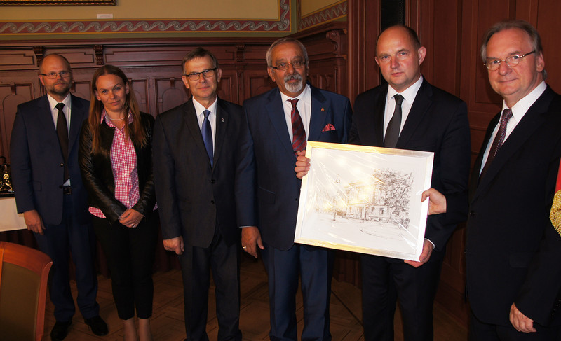 Das Foto zeigt rechts Ministerpräsident Haseloff, der Marschall Całbecki (links neben ihm) eine gerahmte Federzeichnung des Palais am Fürstenwall überreicht. Links daneben sind die vier weiteren Delegationsmitglieder abgebildet.
