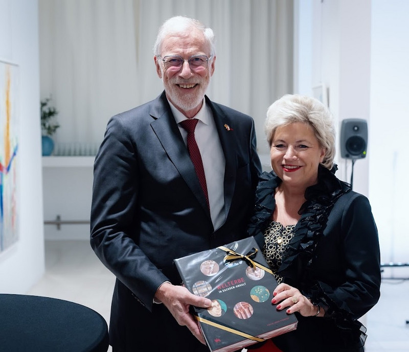 Das Foto zeigt Herrn Minister Robra (links) bei der Überreichung eines Bildbandes zum Welterbe Sachsen-Anhalt an Frau Generalkonsulin Pieper (rechts). Beide lächeln in die Kamera.
