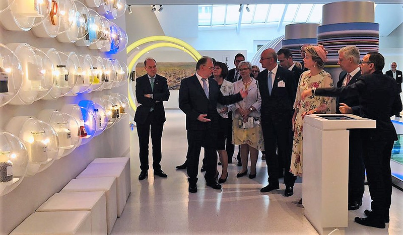 Das Bild zeigt unter anderem das Königspaar im Besucherzentrum des Chemieparks Leuna, wo es eine Ausstellungswand mit hier hergestellten Produkten betrachtet.