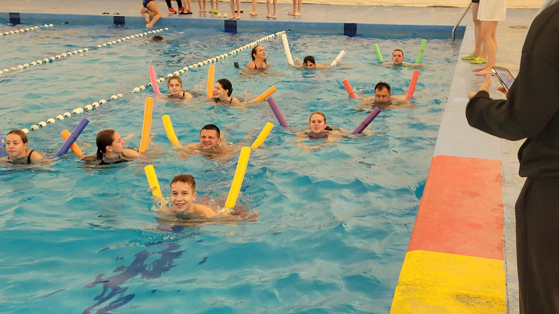 Jugendliche schwimmen mit Poolnudel in einem Schwimmbecken.
