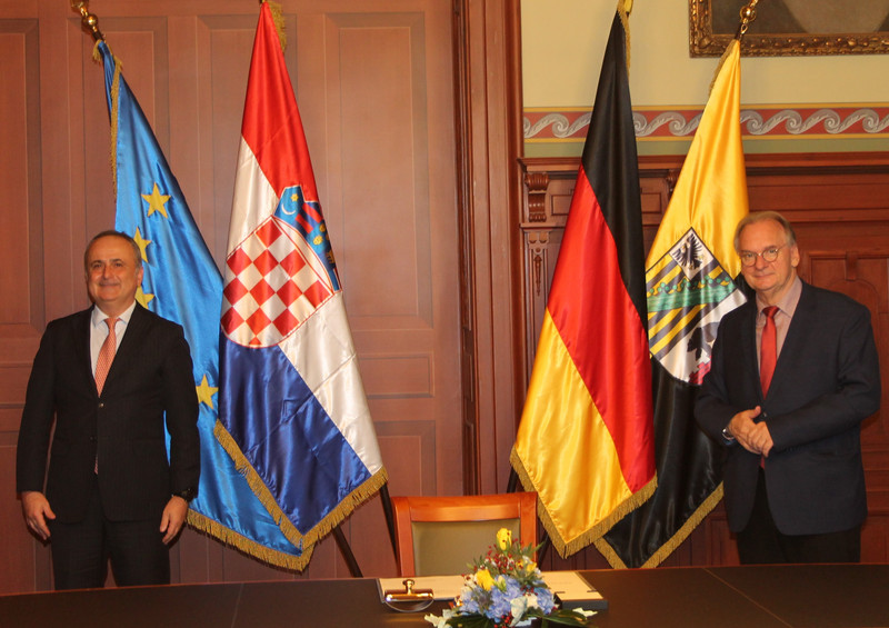 Das Bild zeigt den Botschafter der Republik Kroatien, Gordan Bakota (links), und Ministerpräsident Dr. Reiner Haseloff (rechts). Im Hintergrund sind die Fahnen der EU, Sachsen-Anhalts und Kroatiens zu sehen.