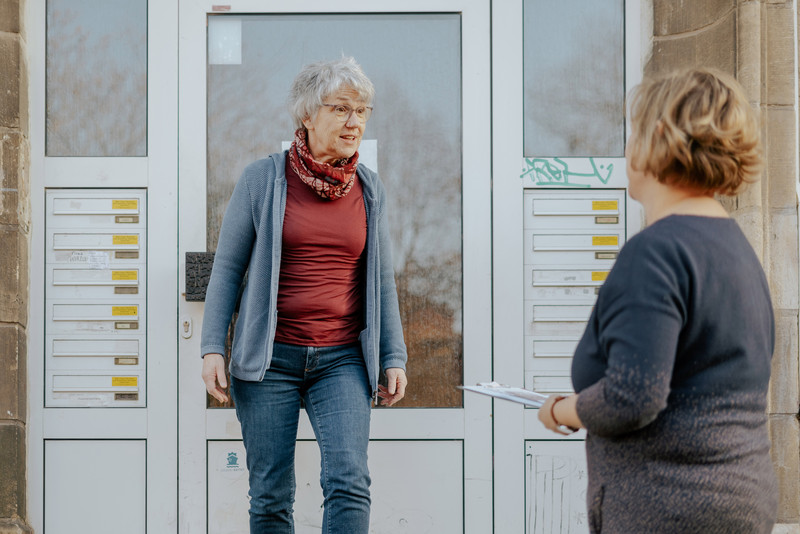 Das Foto zeigt zwei Frauen vor einer Haustür. 