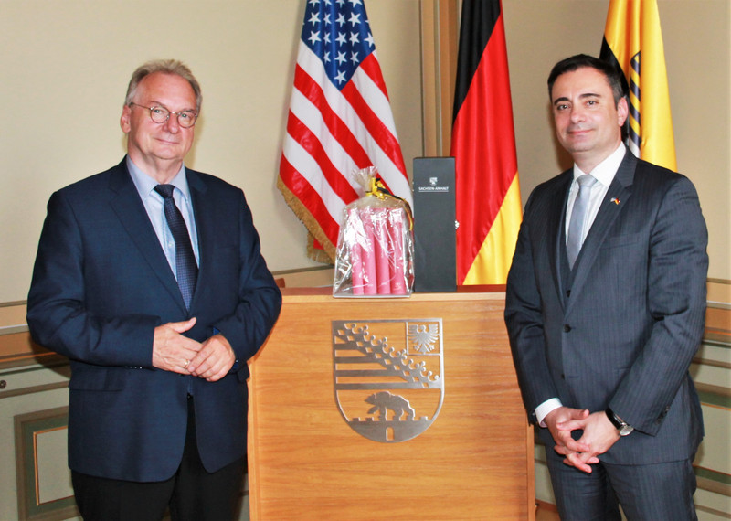 Das Bild zeigt links Ministerpräsident Reiner Haseloff und rechts Generalkonsul Timothy Eydelnant vor den Fahnen der USA, Deutschlands und Sachsen-Anhalts.