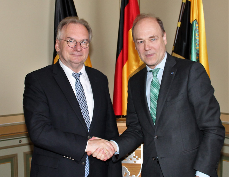 Das Bild zeigt links Ministerpräsident Haseloff und rechts Botschafter Van de Voorde beim Handschlag zur Begrüßung vor den Fahnen Belgiens, Deutschlands und Sachsen-Anhalts.