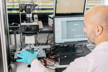 Das Foto zeigt einen Mitarbeiter am Computer und Mikroskop. 