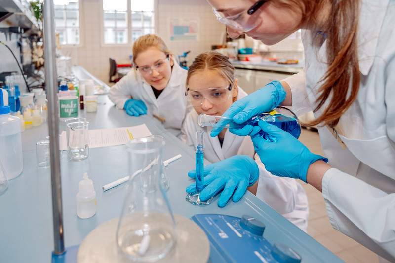 Das Bild zeigt drei Mädchen bei einem Experiment in einem Labor. 